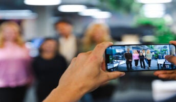 Person taking a picture of a group of people on their mobile. Source: Tech.co