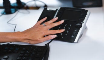 Hand typing on desk phone dialpad. Source: Tech.co