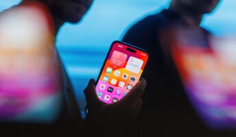 Man holding iPhone 15 Pro against shadowy background illustrating iPhone spyware threat