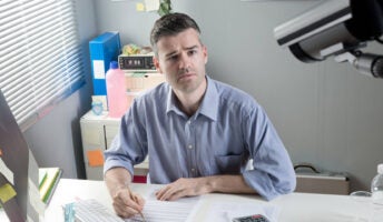 A man working remotely at his desk being spied on by his employer and CCTV