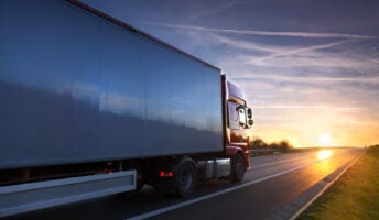 A large red truck drives toward the sunset on open road