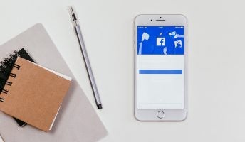 notepads with a pen and facebook on a mobile device showing a thumbs down