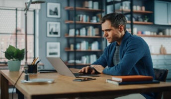 A man sitting at a desk looking at a laptop screen