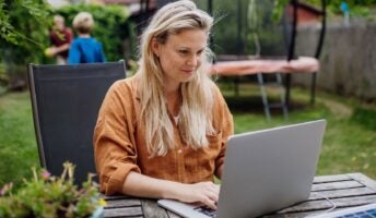 Woman remote working in her backyard with her two kids playing in the background.