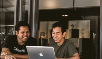 two men smiling at a laptop in a small office