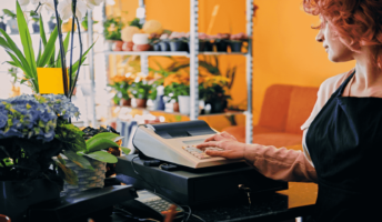 A woman in a small florist uses a cash register.